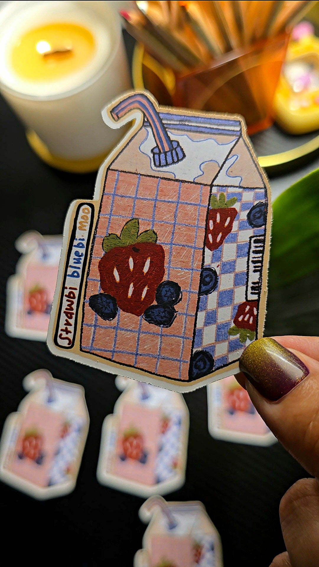 Cartoon milk carton sticker with strawberry and blueberry design held by a hand.