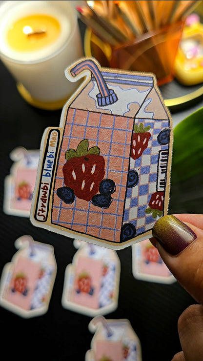 Cartoon milk carton sticker with strawberry and blueberry design held by a hand.