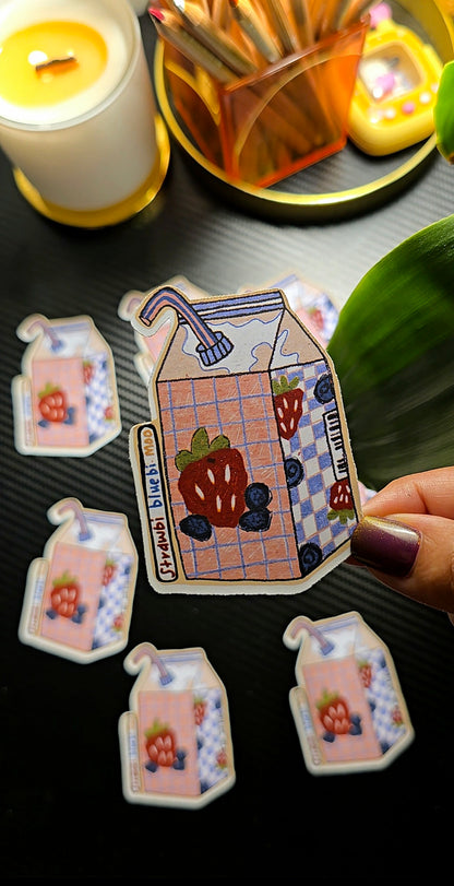 Decorative house-shaped stickers with a person holding one, on a dark surface with candles and a plant.