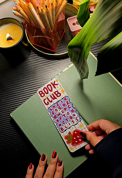 Book Club Word Search holographic bookmark held open in a book showing grid design and strawberry at the bottom