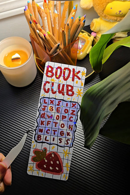 Book Club Word Search holographic bookmark flat lay showing word search grid with BLISS hidden word and strawberry illustration