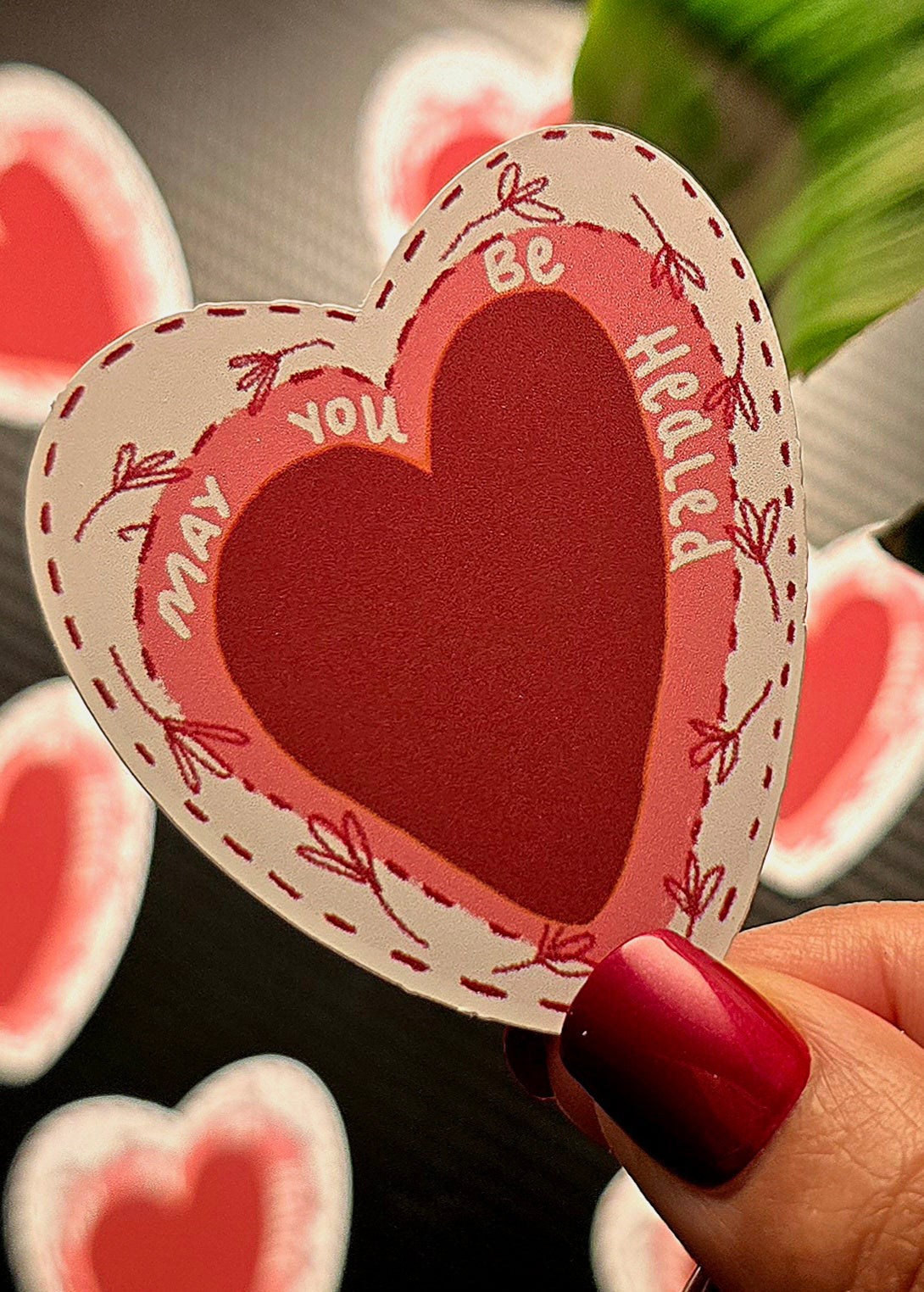 Heart-shaped card with 'May you be healed' text held by a hand with red nail polish.