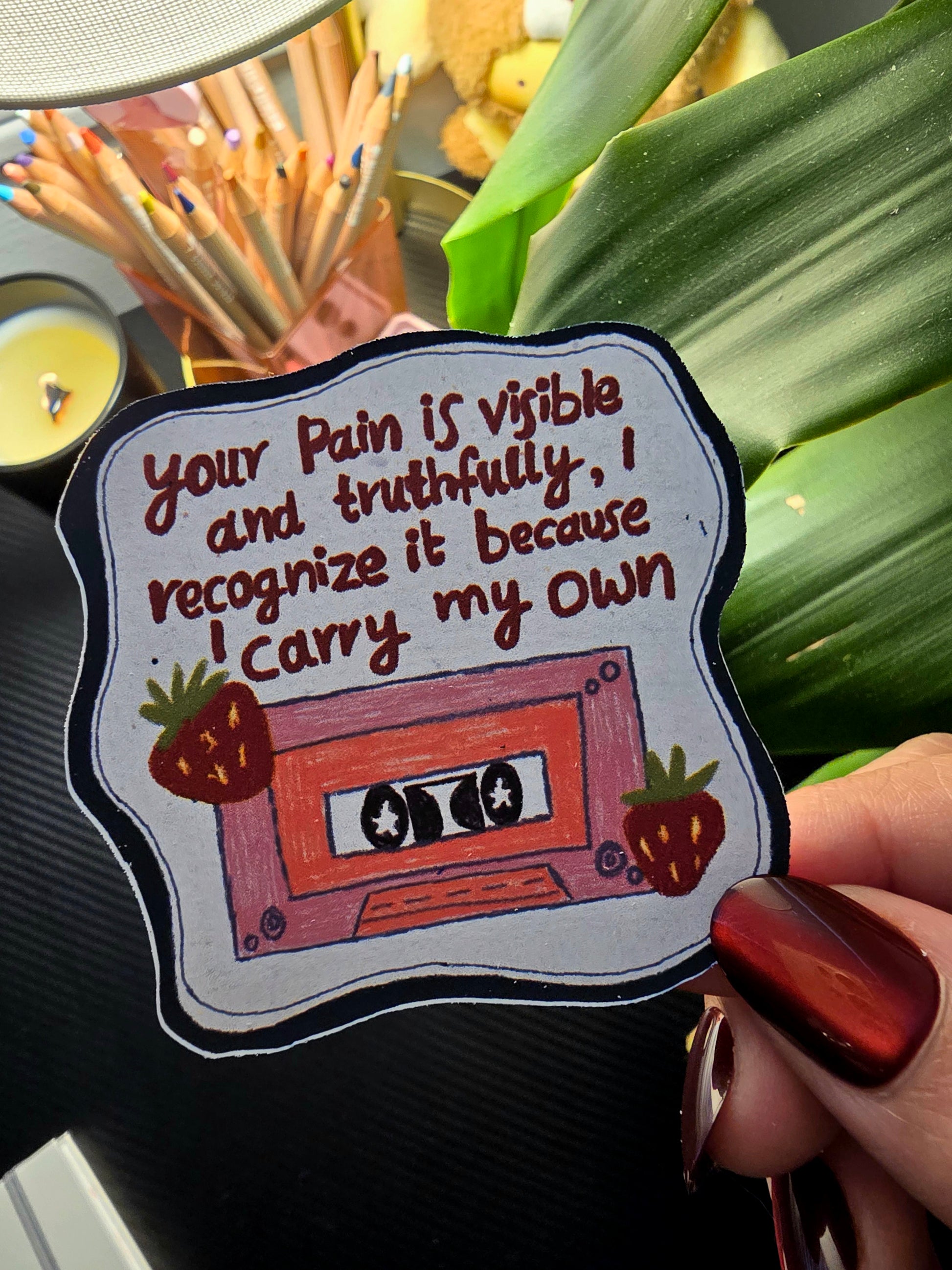 Decorative keychain with a cassette tape design and text, held by a hand.