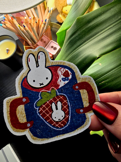 Decorative patch with a rabbit design held by a hand, surrounded by stationery items.