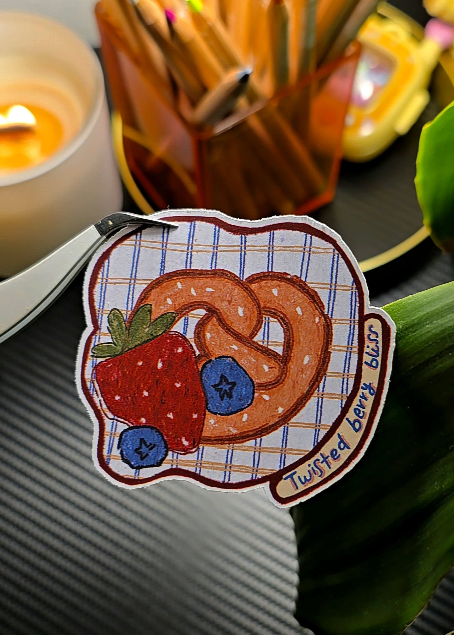 Twisted Berry Bliss die-cut sticker featuring a pretzel heart with strawberry and blueberries on a plaid background